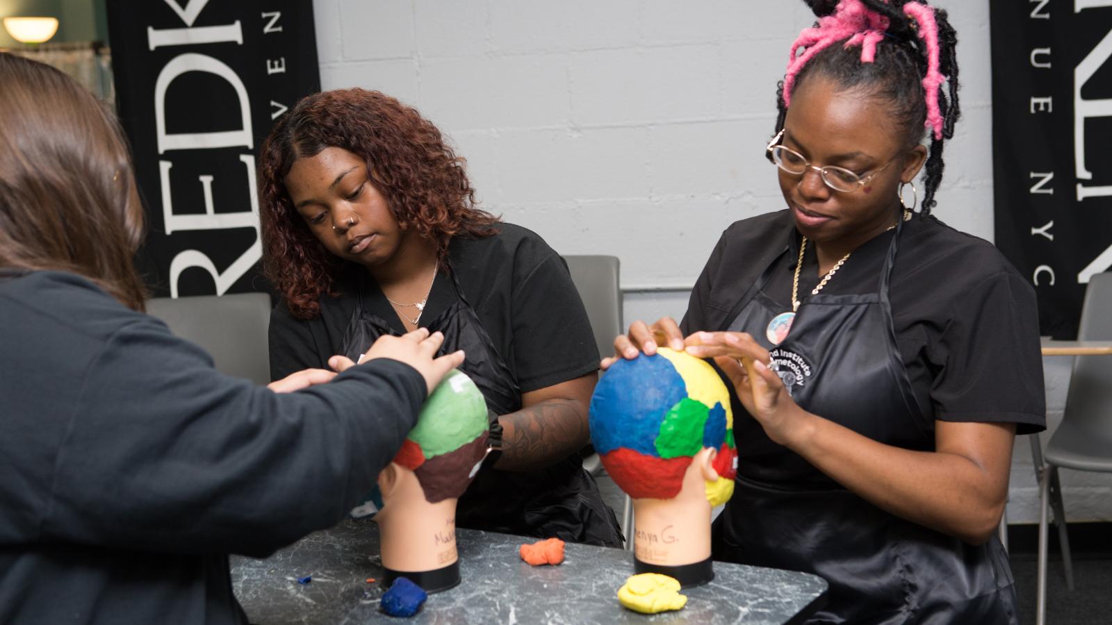 Two students putting red, blue, green, and yellow clay on the scalp of a manikin